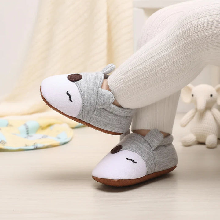 Gray and white animal-face baby shoes worn with ribbed cream pants.