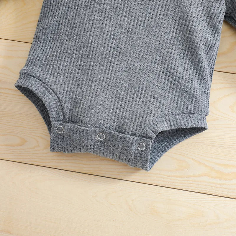 Close-up of bottom snap closures and textured fabric on a gray baby bodysuit