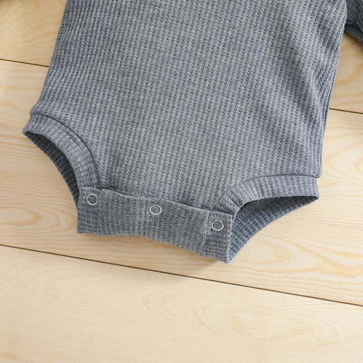 Close-up of bottom snap closures and textured fabric on a gray baby bodysuit