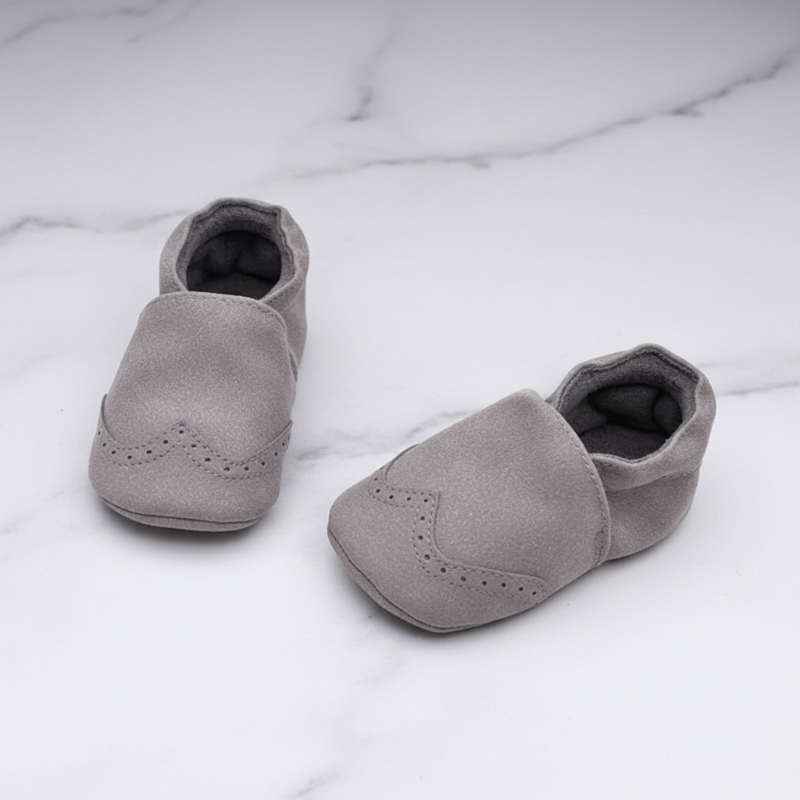 Gray baby shoes with gathered ankles and decorative toe details on a marble-patterned surface