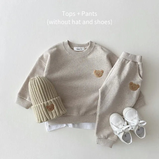 Gray sweatshirt and cuffed pants with bear patches, arranged with a knit hat and white shoes