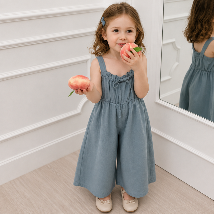 Child wearing the gray sleeveless bow jumpsuit beside a mirror