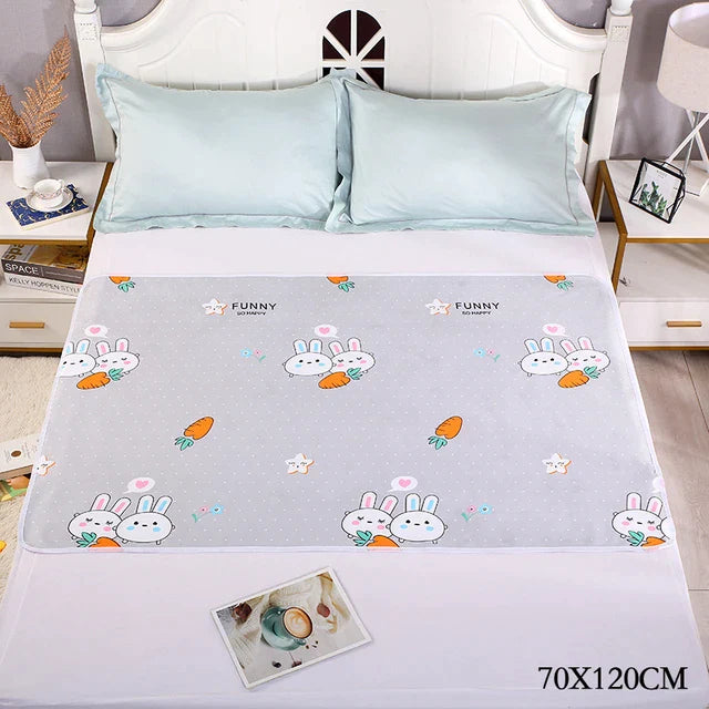 Gray changing mat with bunnies and carrots on a bed, labeled 70 x 120 cm.