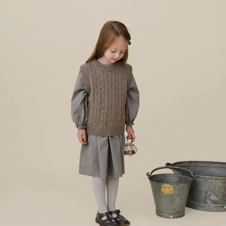 Child wearing a gray cable-knit vest over a gray dress