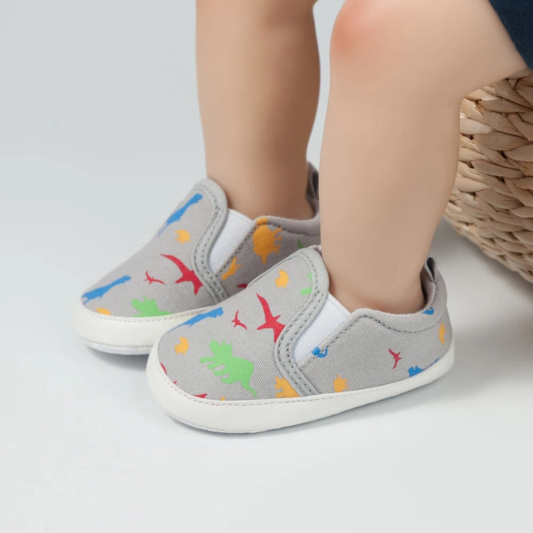 Gray dinosaur-print baby sneakers with white soles, shown on feet