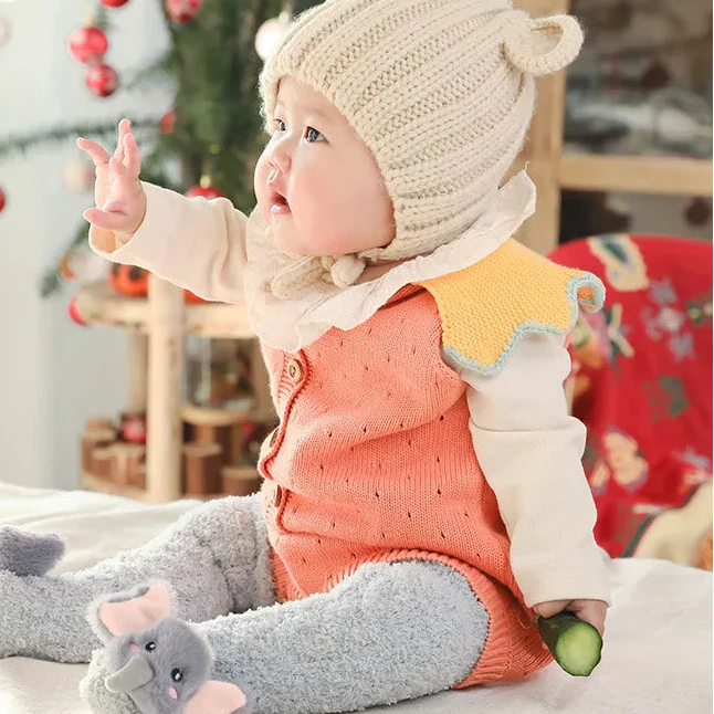 Seated baby wearing long gray socks with elephant faces and pink ears.