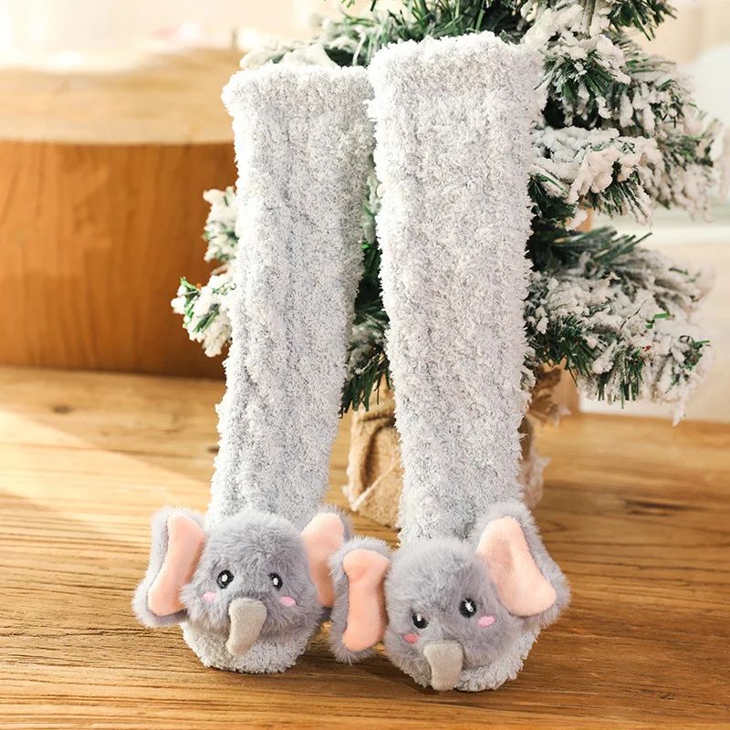 Gray long baby socks with elephant faces and pink ears beside a small tree.