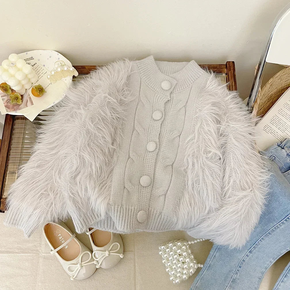 Gray winter coat with ribbed cuffs, a cable-knit front and fluffy panels, laid over jeans.