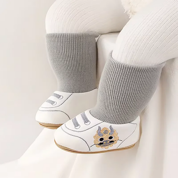 White baby shoes with tall gray knit cuffs worn with cream leggings.