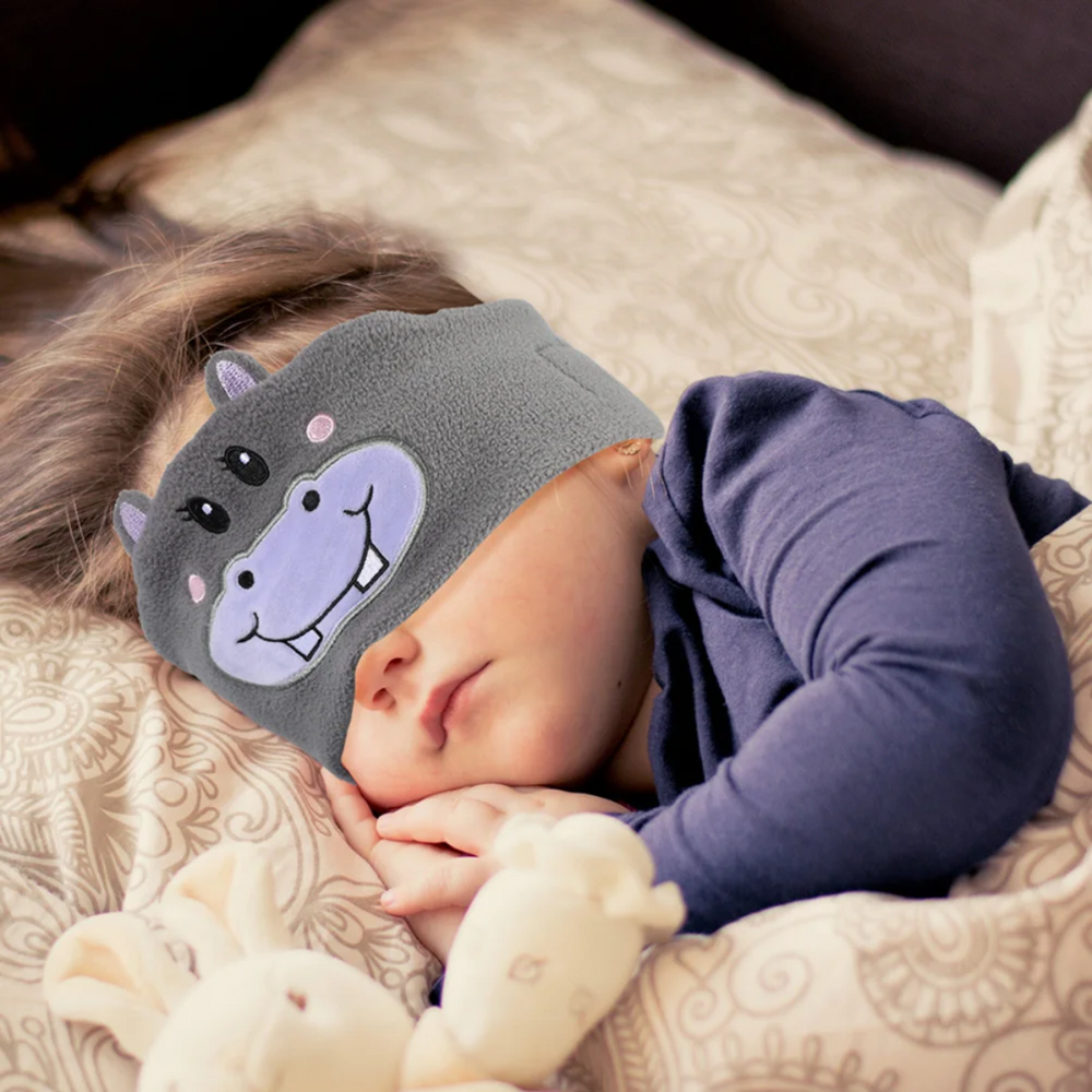 Child resting on a pillow while wearing the gray hippopotamus Bluetooth sleep mask.