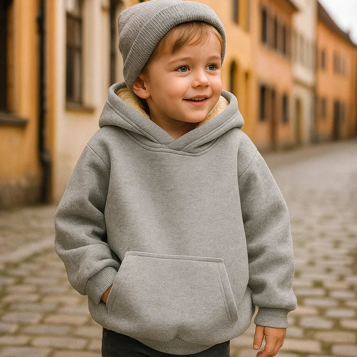 Child wearing a gray hoodie with a front pouch pocket and a knit hat on a cobblestone street