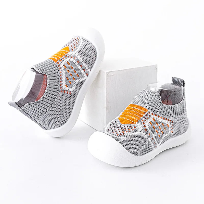 Gray knit baby shoes shown from the side with orange accents and white soles