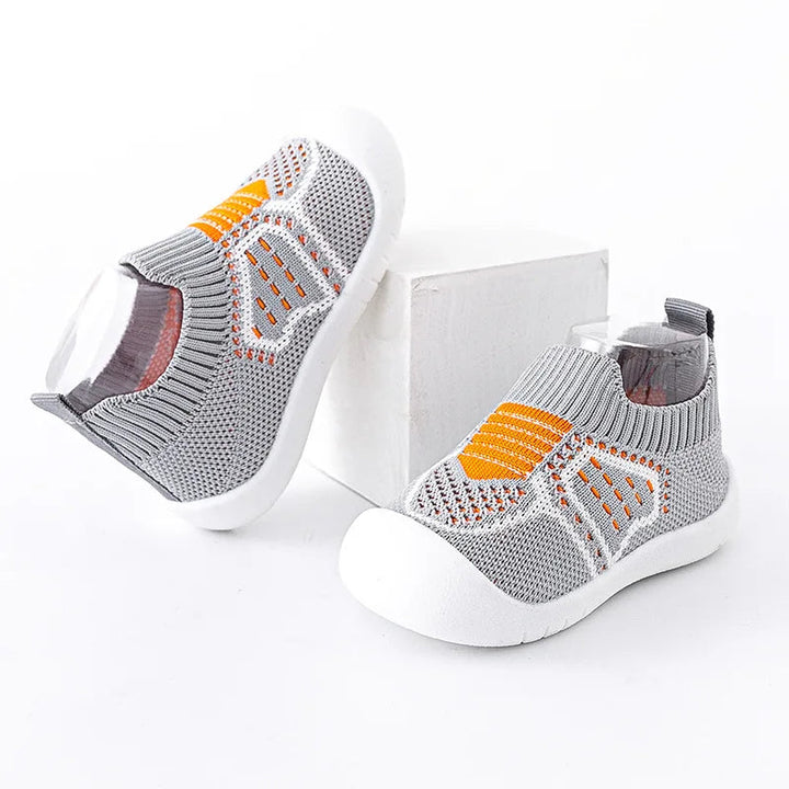 Gray knit baby shoes shown from the side with orange accents and white soles