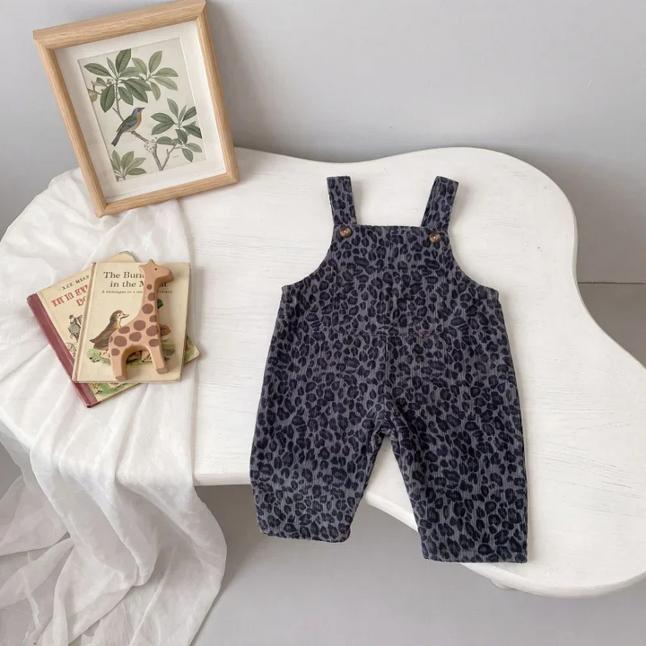 Gray leopard print overalls laid out on a curved white chair beside books