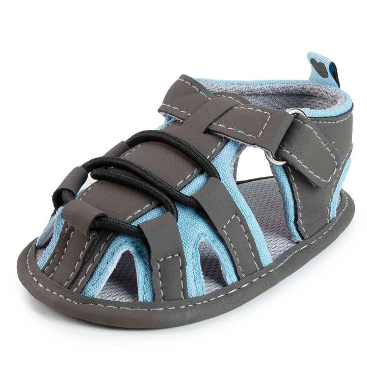 Gray baby sandal with light blue trim, black front cords and an ankle strap