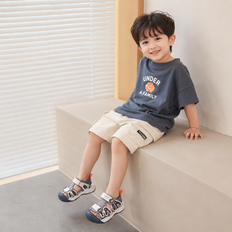 Child seated on a bench wearing gray and navy closed-toe sandals