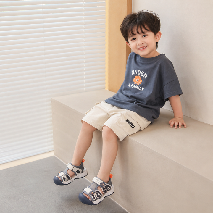 Child seated on a bench wearing gray and navy closed-toe sandals