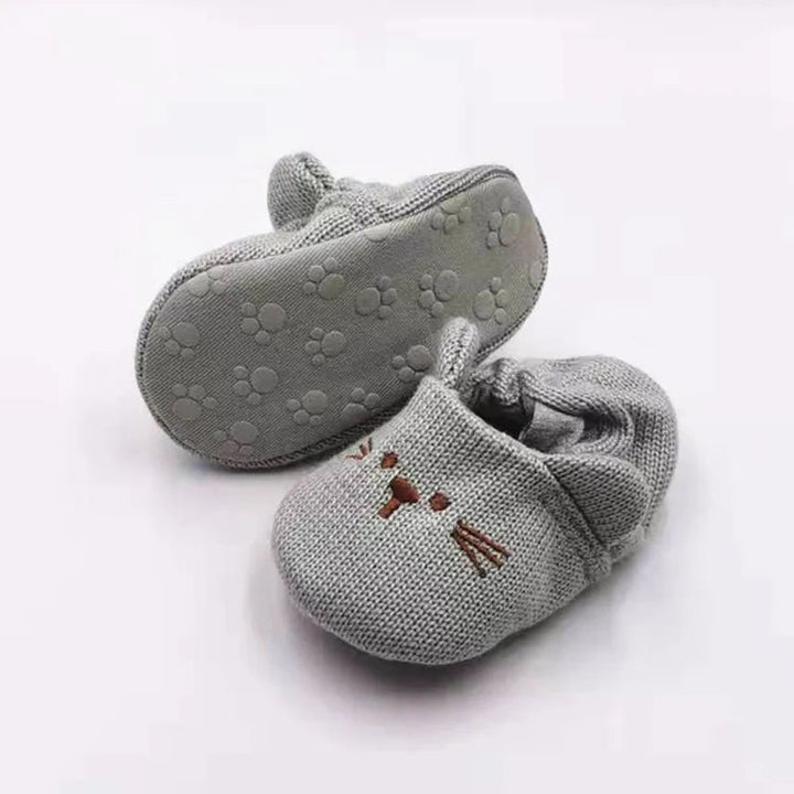 Gray rabbit baby slippers showing an embroidered face and a paw-patterned sole