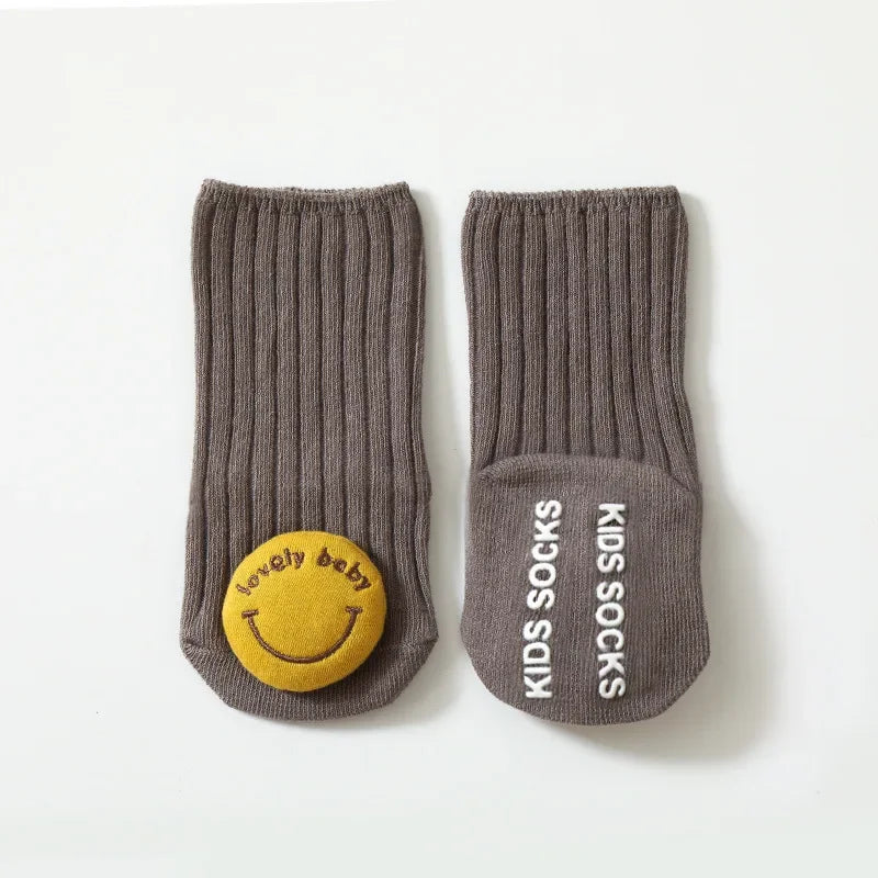 Gray baby socks with a yellow smiley face and non-slip sole lettering