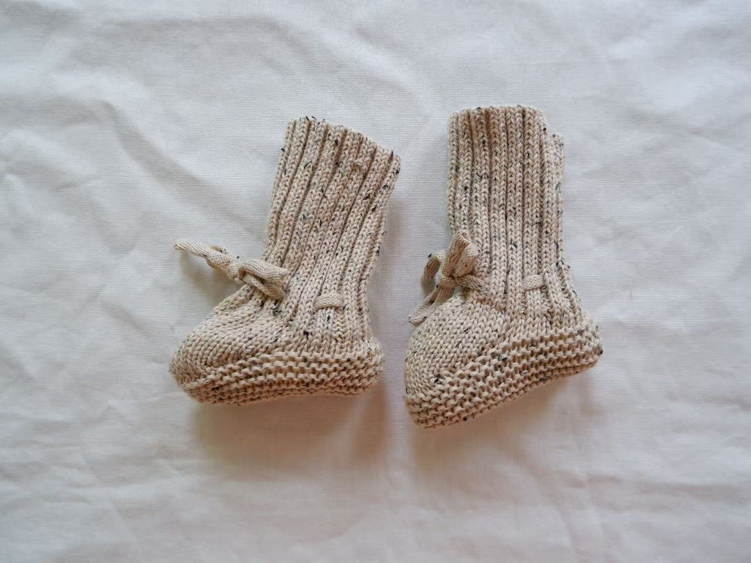 Gray speckled knitted baby booties with tall ribbed cuffs and ankle ties.