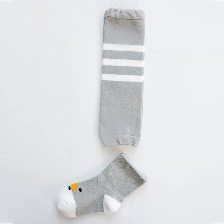 Gray baby leg warmer with white stripes beside a gray bird-face sock with a white toe.