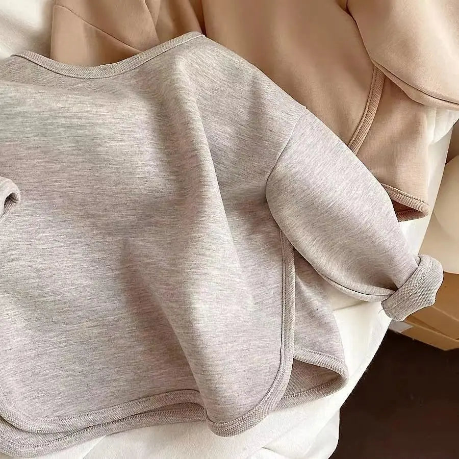 Gray sweater close-up showing the crew neckline, sleeve cuff, and curved hem