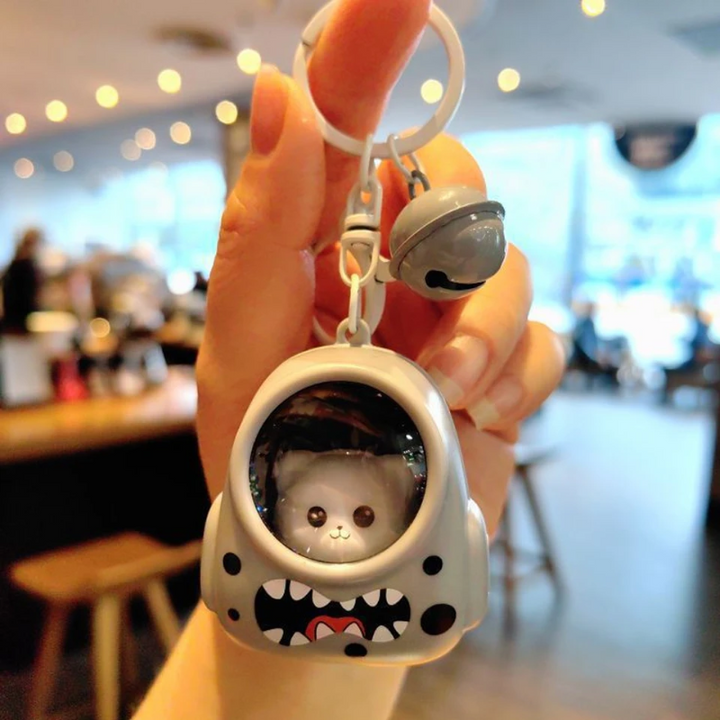 Gray astronaut capsule charm with a toothy face design, key ring, and bell