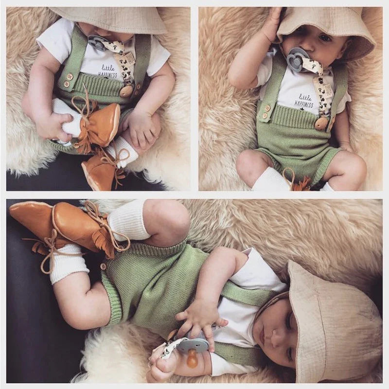 Baby wearing a green knit romper over a white shirt with a tan sunhat