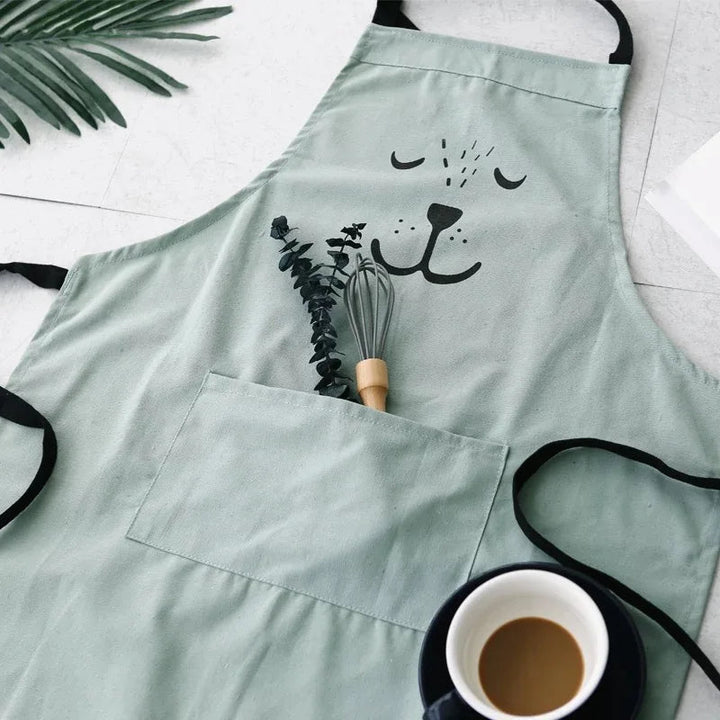 Green bear apron laid flat with black ties, a whisk, and coffee cup
