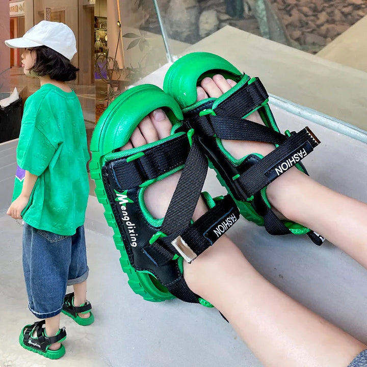 Green sandals with black straps shown on feet and worn with a green shirt and denim outfit.