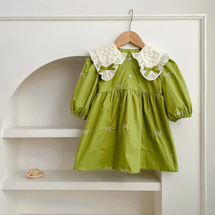 Green dress with a cream ruffled collar and bow details displayed in a white alcove