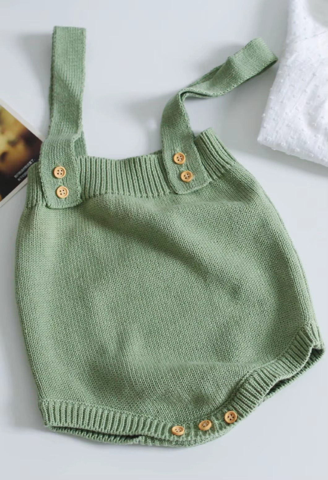 Green knit baby romper with ribbed trim and buttons at the straps and crotch