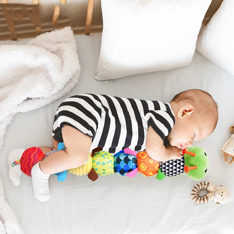 Green caterpillar rattle beside a baby wearing a black-and-white striped outfit