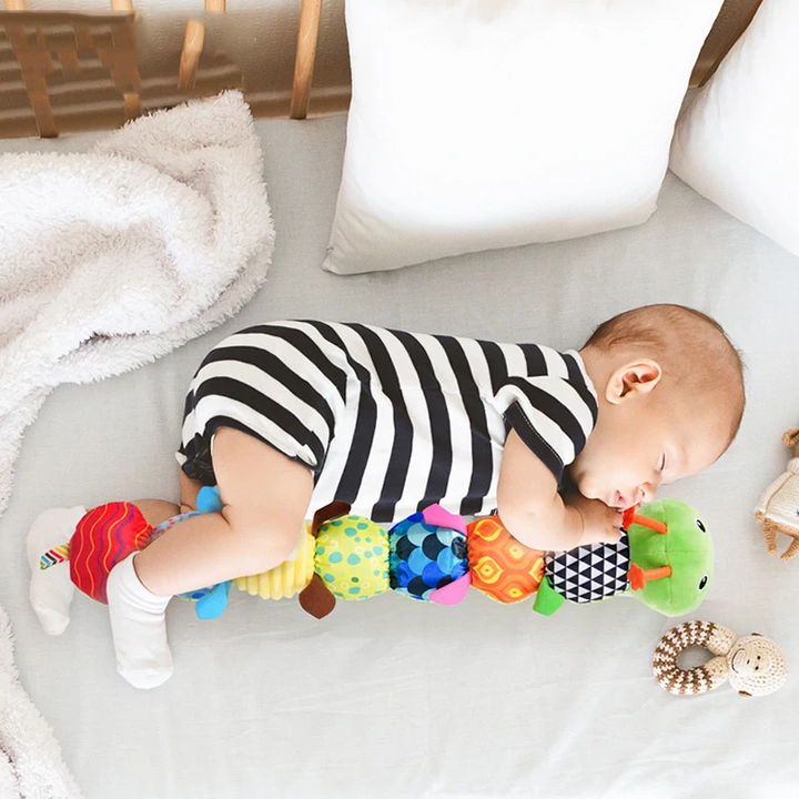 Green caterpillar rattle beside a baby wearing a black-and-white striped outfit