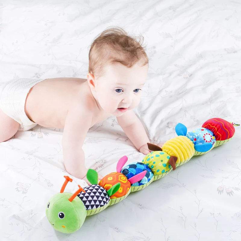 Baby reaching toward a green caterpillar rattle during tummy time