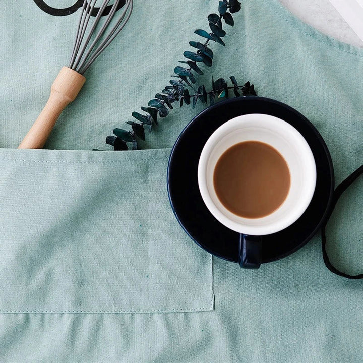Green cotton apron with a front pocket, whisk, and coffee cup