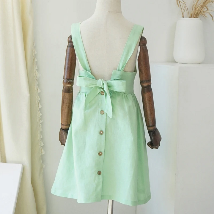 Back view of the green dress on a mannequin, showing the tied bow and decorative button row