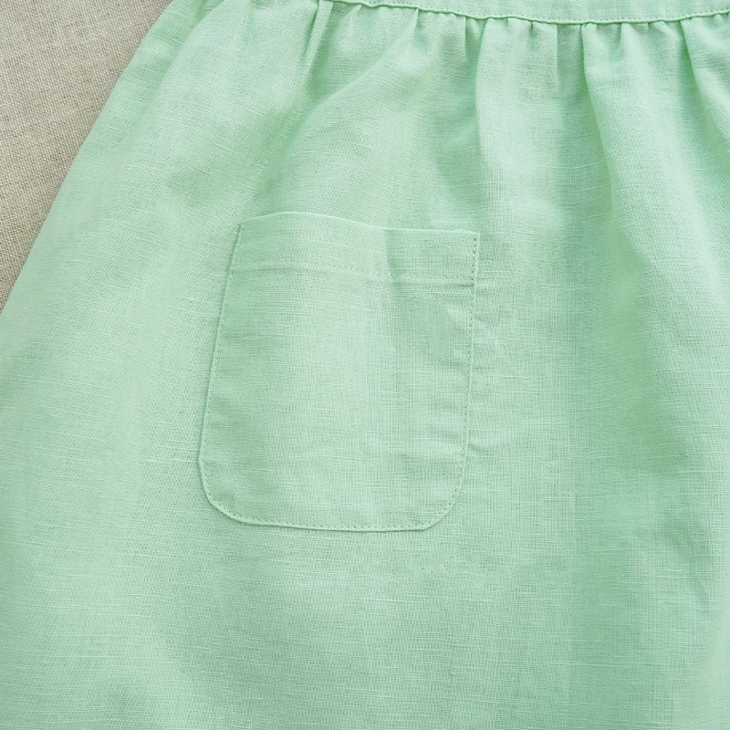 Close-up of a front patch pocket and gathered waist on the green cotton dress