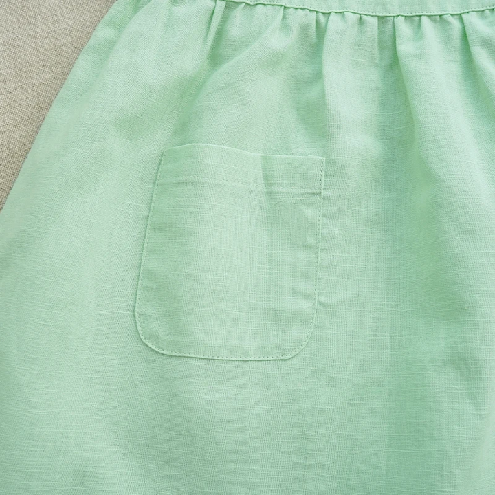 Close-up of a front patch pocket and gathered waist on the green cotton dress