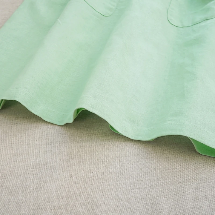 Green cotton skirt detail showing the hem and lower edges of the front pockets