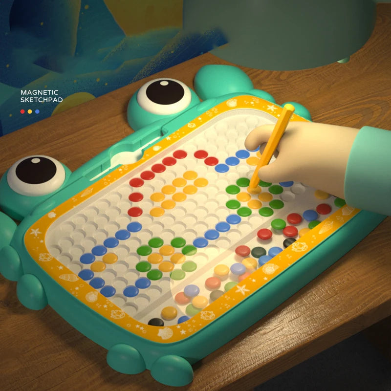 Hand using a yellow magnetic pen to move beads on a green crab-shaped drawing board