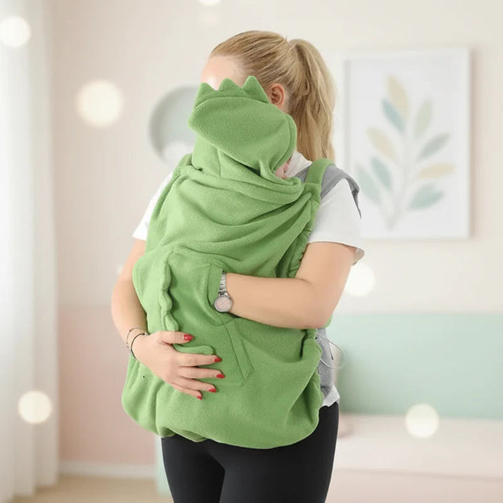 Green hooded dinosaur cover wrapped around a front baby carrier indoors
