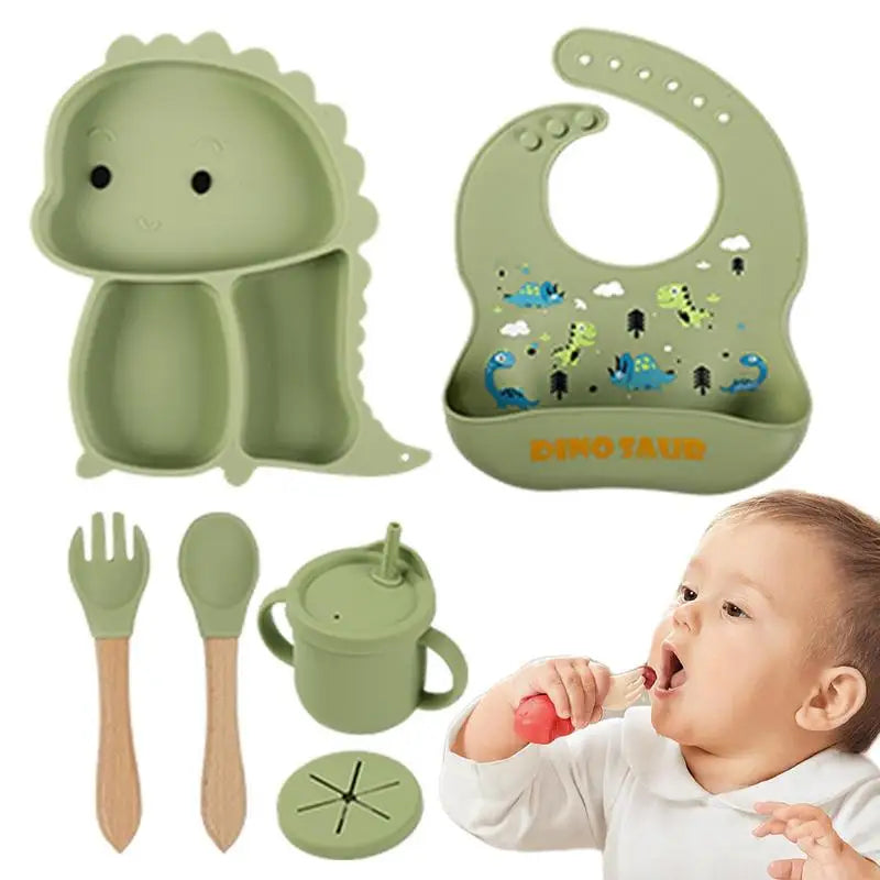 Green dinosaur tableware set with bib, handled cup, utensils, two lids, and a child drinking