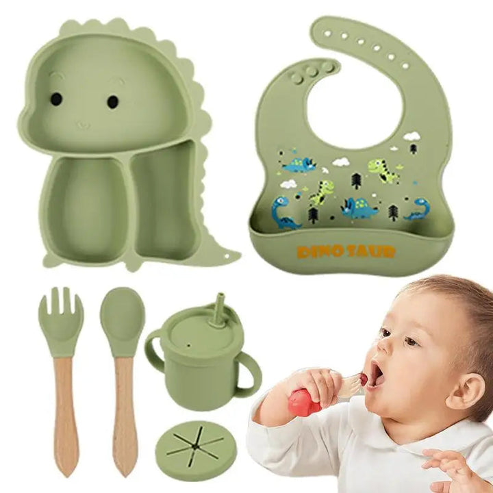 Green dinosaur tableware set with bib, handled cup, utensils, two lids, and a child drinking