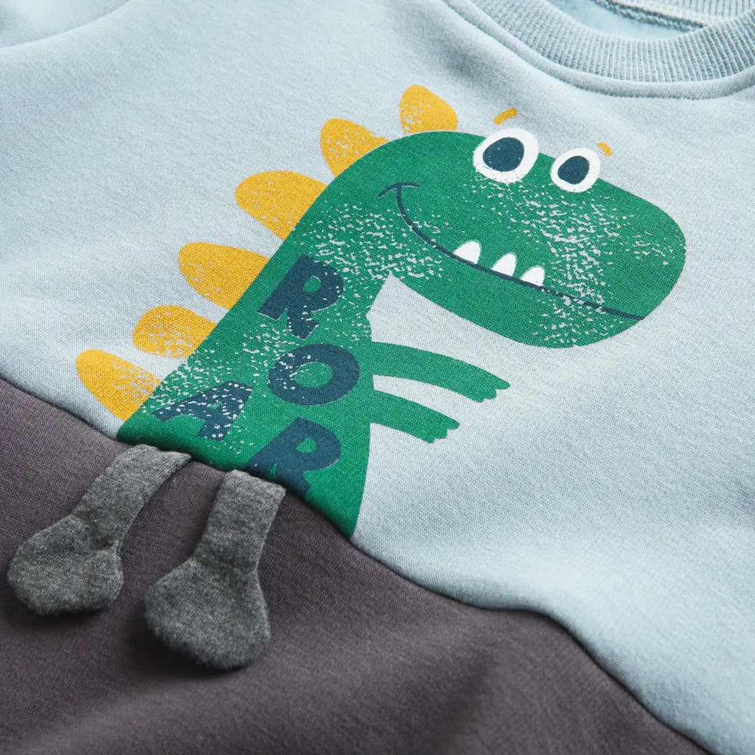Close-up of the green dinosaur print and fabric accents on the blue cotton romper