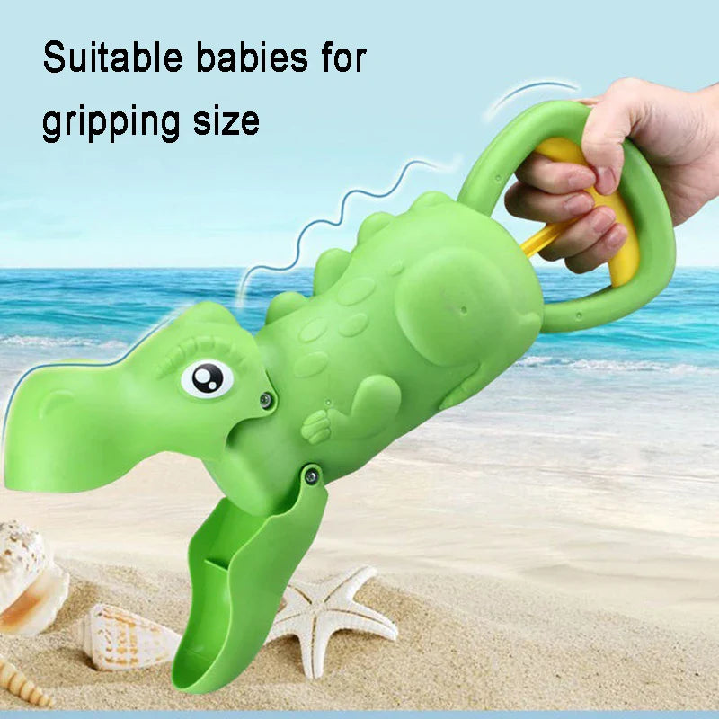Hand holding a green dinosaur sand grabber by its loop handle at the beach
