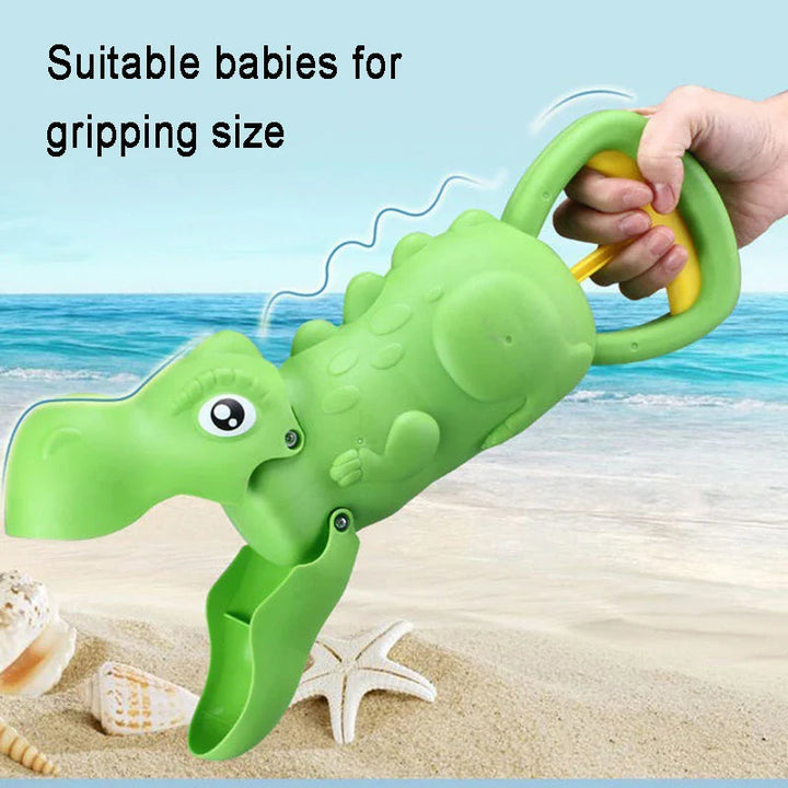 Hand holding a green dinosaur sand grabber by its loop handle at the beach