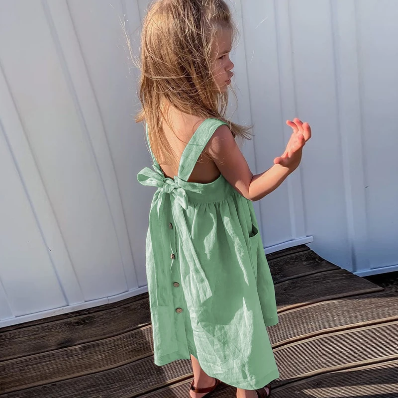 Child wearing the green cotton dress, viewed from behind with the bow and buttons visible