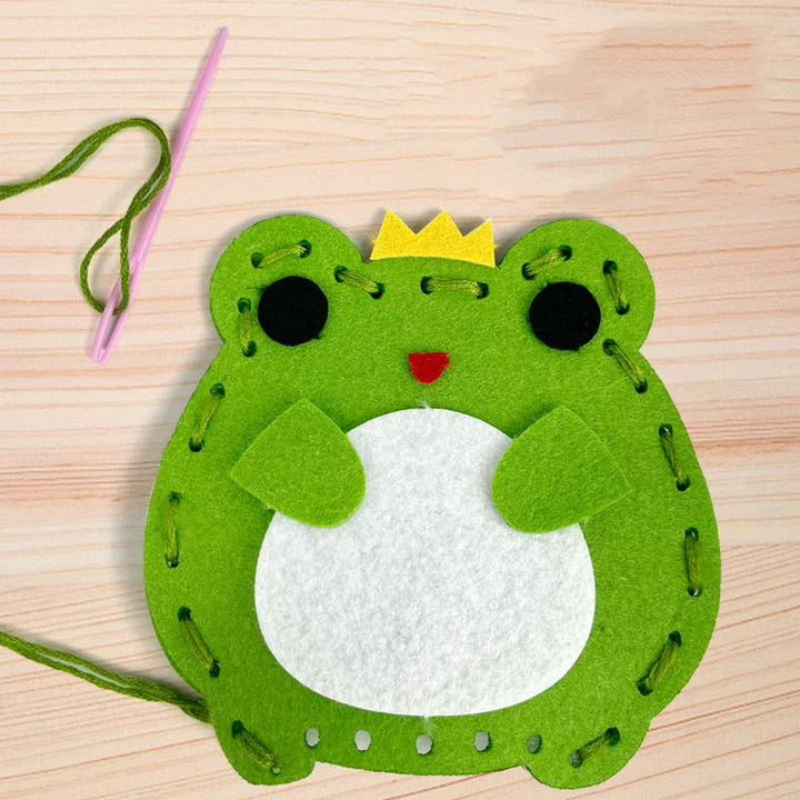 Green felt frog with a yellow crown beside a plastic needle and green thread