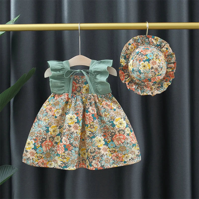 Floral baby dress with green ruffled straps and a coordinating hat on a hanging display